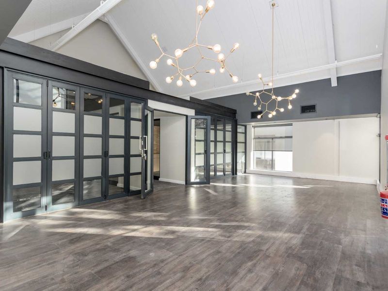 Spacious office area featuring vaulted ceilings, modern pendant lighting, and stylish frosted glass partition doors with durable laminate flooring.