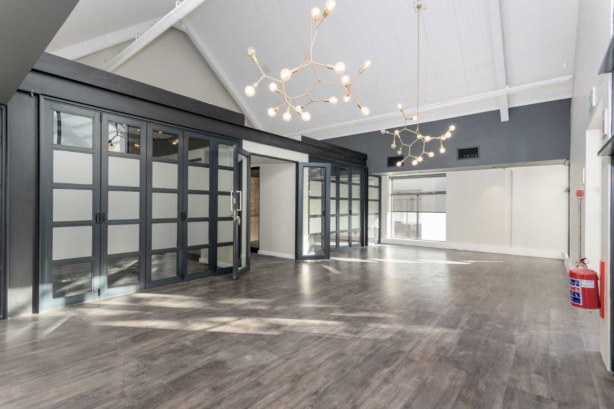 Spacious office area featuring vaulted ceilings, modern pendant lighting, and stylish frosted glass partition doors with durable laminate flooring.