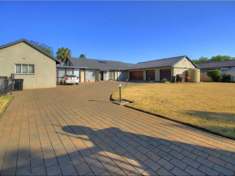 Spacious front exterior featuring a large paved driveway, triple garage, and a well-defined lawn area with a water tank.