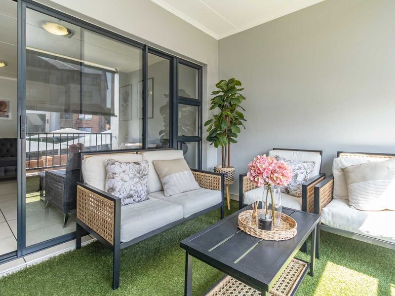 A well-maintained covered balcony featuring artificial grass flooring and large sliding glass doors providing access to the interior living space.