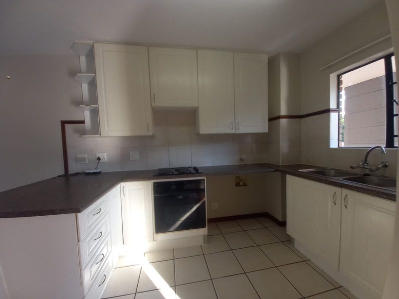 A functional kitchen featuring white built-in cabinetry, laminate countertops, a built-in oven with gas hob, and tiled flooring.