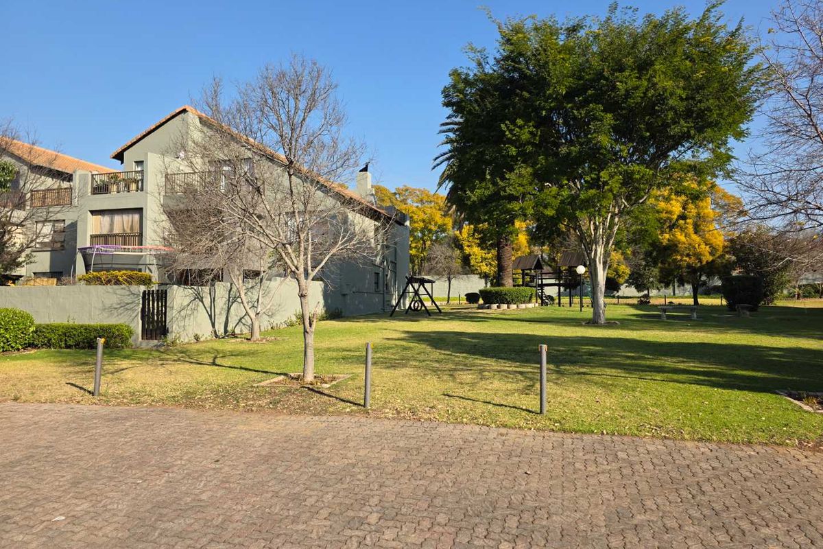 A view of the apartment complex exterior featuring a well-maintained communal garden, paved driveway, and private balconies.