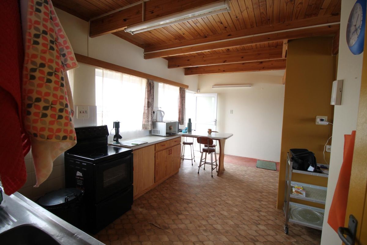 A functional kitchen featuring timber ceiling beams, wooden cabinetry, a freestanding stove, and vinyl flooring with an integrated breakfast bar area.