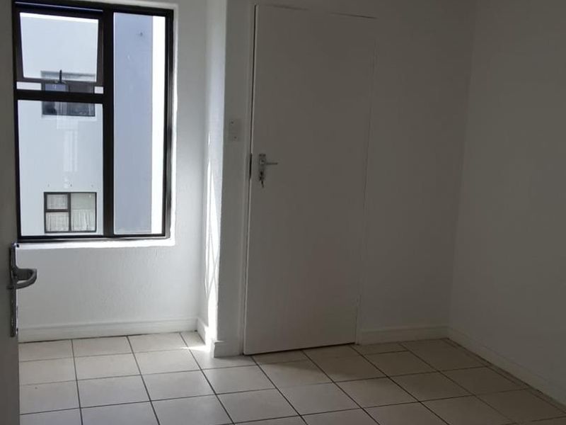 A vacant bedroom featuring neutral tiled flooring, a single window with an aluminium frame, and a simple interior door.