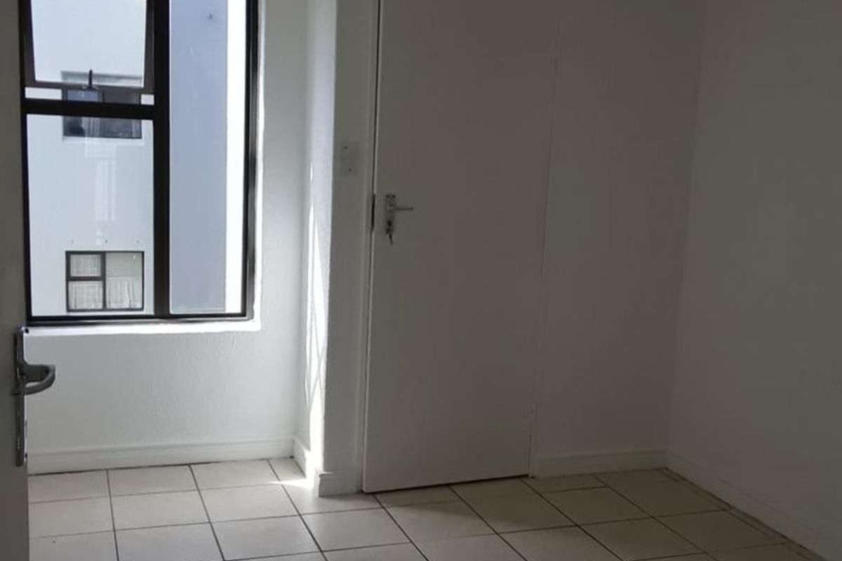 A vacant bedroom featuring neutral tiled flooring, a single window with an aluminium frame, and a simple interior door.