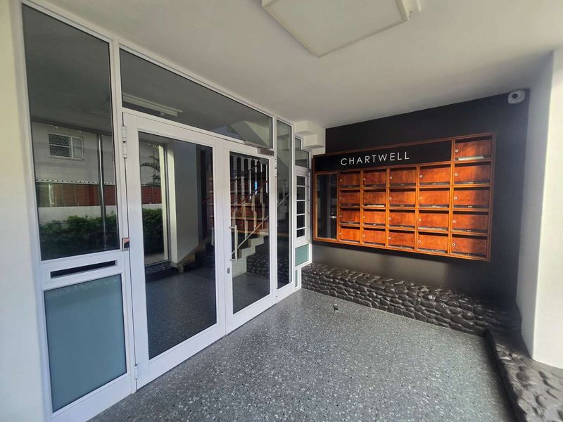 A clean and well-maintained apartment building entrance featuring a glass door, built-in wooden mailboxes, and decorative stone wall accents.