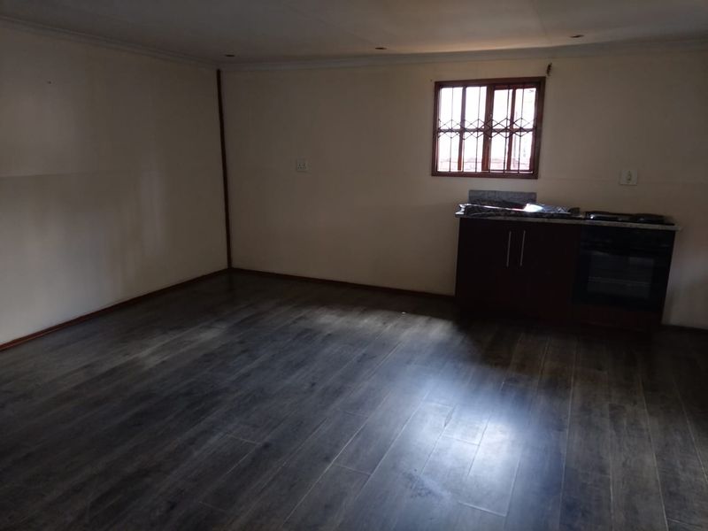 An empty kitchen area featuring dark laminate flooring, built-in cabinetry with an integrated oven and hob, and a window with security bars.