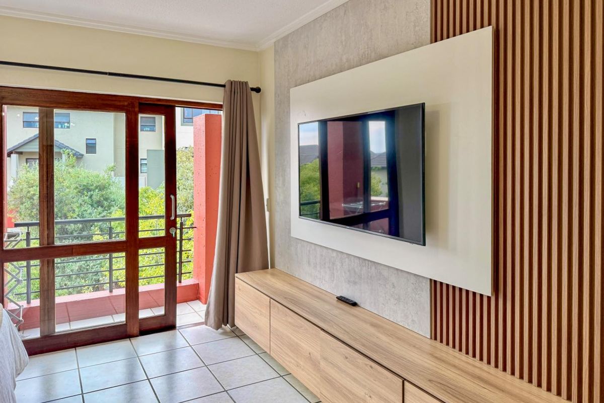 A modern living area featuring a custom timber-slat feature wall, built-in cabinetry, and direct access to a private balcony through a wooden sliding door.