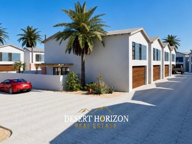 A modern townhouse complex featuring paved driveways, multiple garage units, and clean architectural lines in a desert-inspired residential setting.