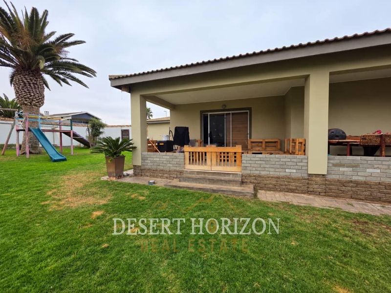A covered patio area featuring a brick base wall and sliding glass door access, overlooking a spacious garden with lawn.