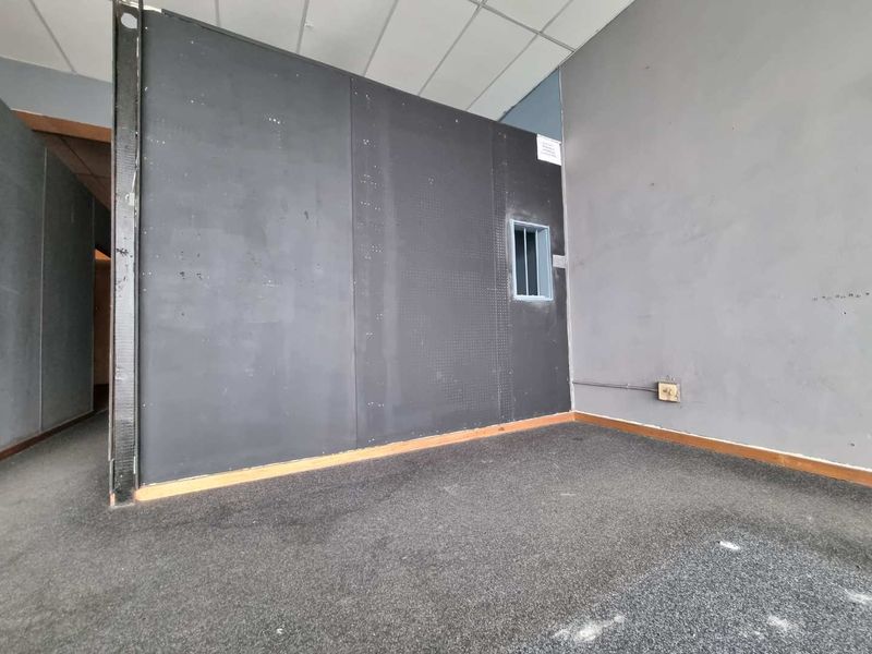 Empty office space featuring dark partition walls, carpeted flooring, and a small security window, suitable for commercial renovation or fit-out.