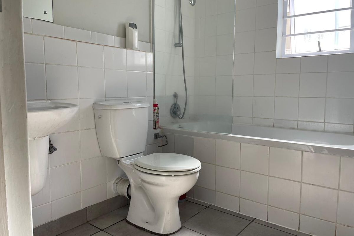 A functional bathroom featuring a white bathtub with shower attachment, pedestal basin, and toilet, finished with white wall tiles and tiled flooring.