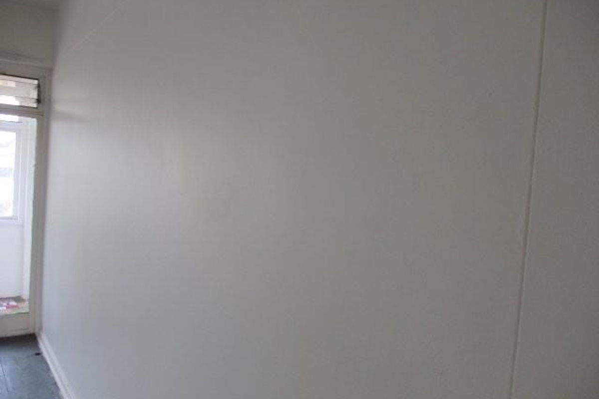 An empty, neutrally painted room featuring simple skirting boards and access to an adjacent outdoor area through a glass door.