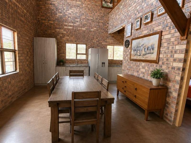 Spacious open-plan dining area featuring high ceilings with exposed timber beams, rustic brick walls, and polished concrete flooring.