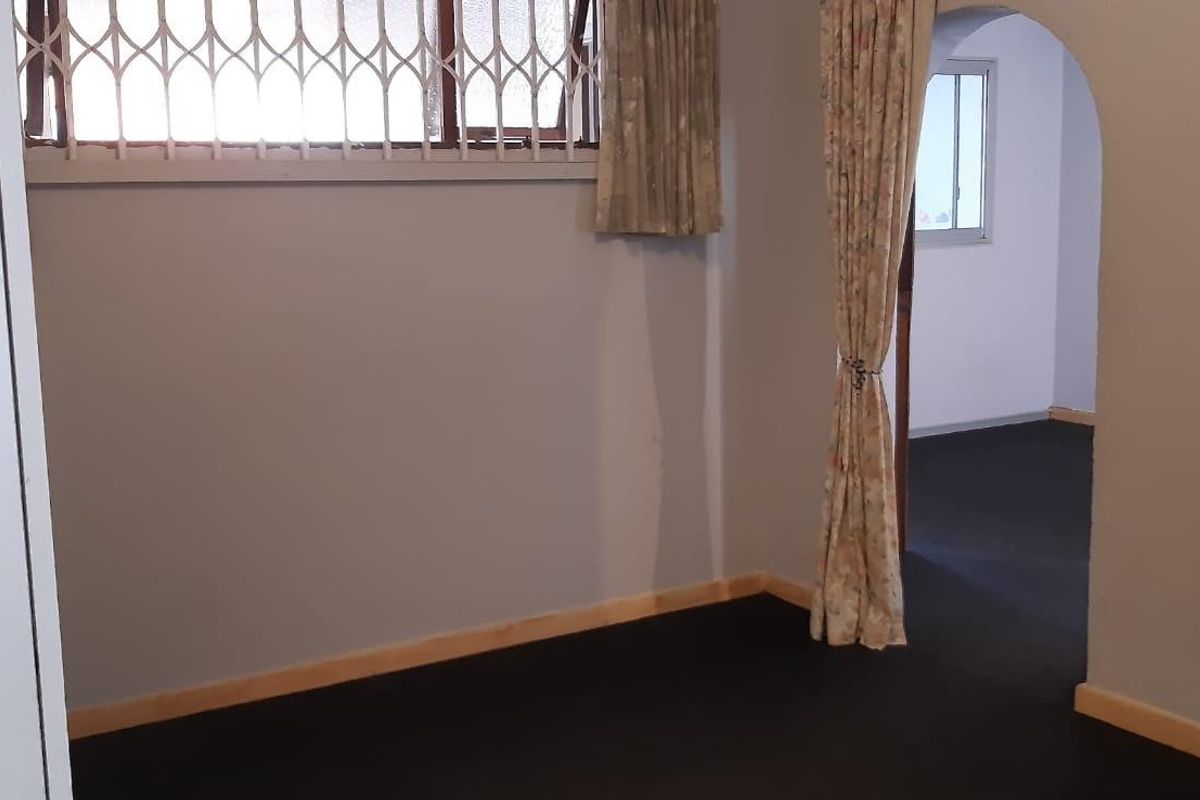 An empty bedroom featuring a security gate on the window, an arched doorway leading to an adjacent room, and built-in storage.