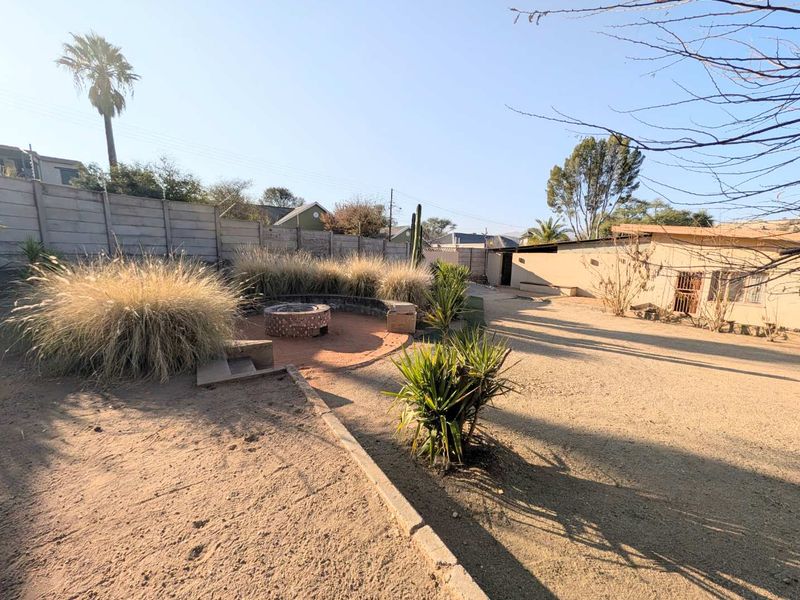 Spacious rear garden area featuring a built-in fire pit, concrete boundary wall, and significant potential for landscaping and outdoor entertainment development.
