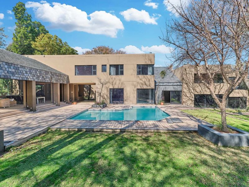 Spacious rear exterior featuring a swimming pool, extensive wooden decking, and a covered patio area set within a landscaped garden.