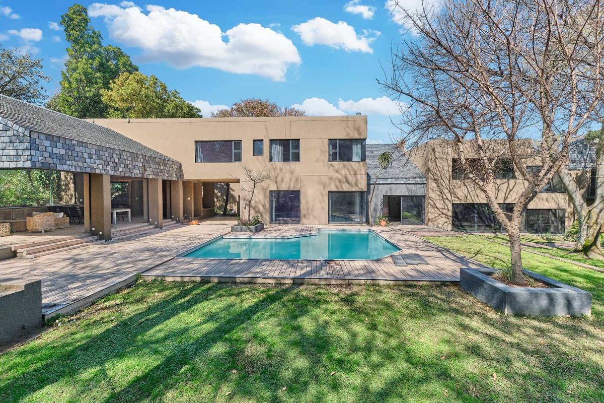 Spacious rear exterior featuring a swimming pool, extensive wooden decking, and a covered patio area set within a landscaped garden.