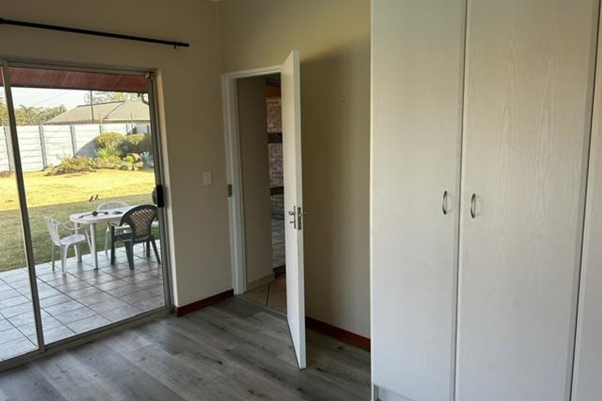 A bright bedroom featuring built-in cupboards, modern laminate flooring, and a sliding glass door providing direct access to the outdoor patio and garden.