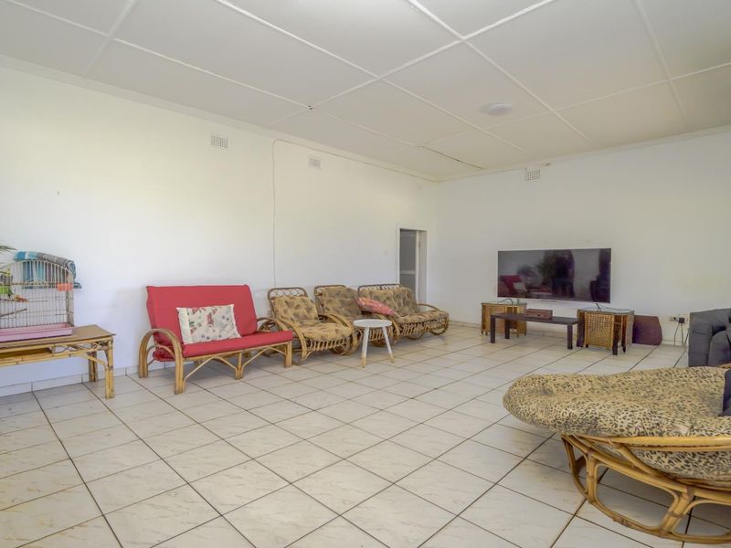 Spacious living room featuring neutral tiled flooring and a panelled ceiling, offering a blank canvas for interior updates.