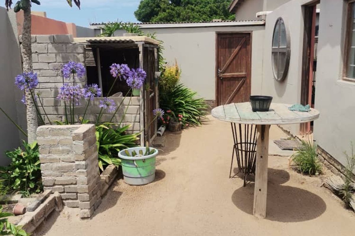 A rear courtyard area featuring a sandy ground surface, perimeter boundary walls, and a small brick-built utility structure.