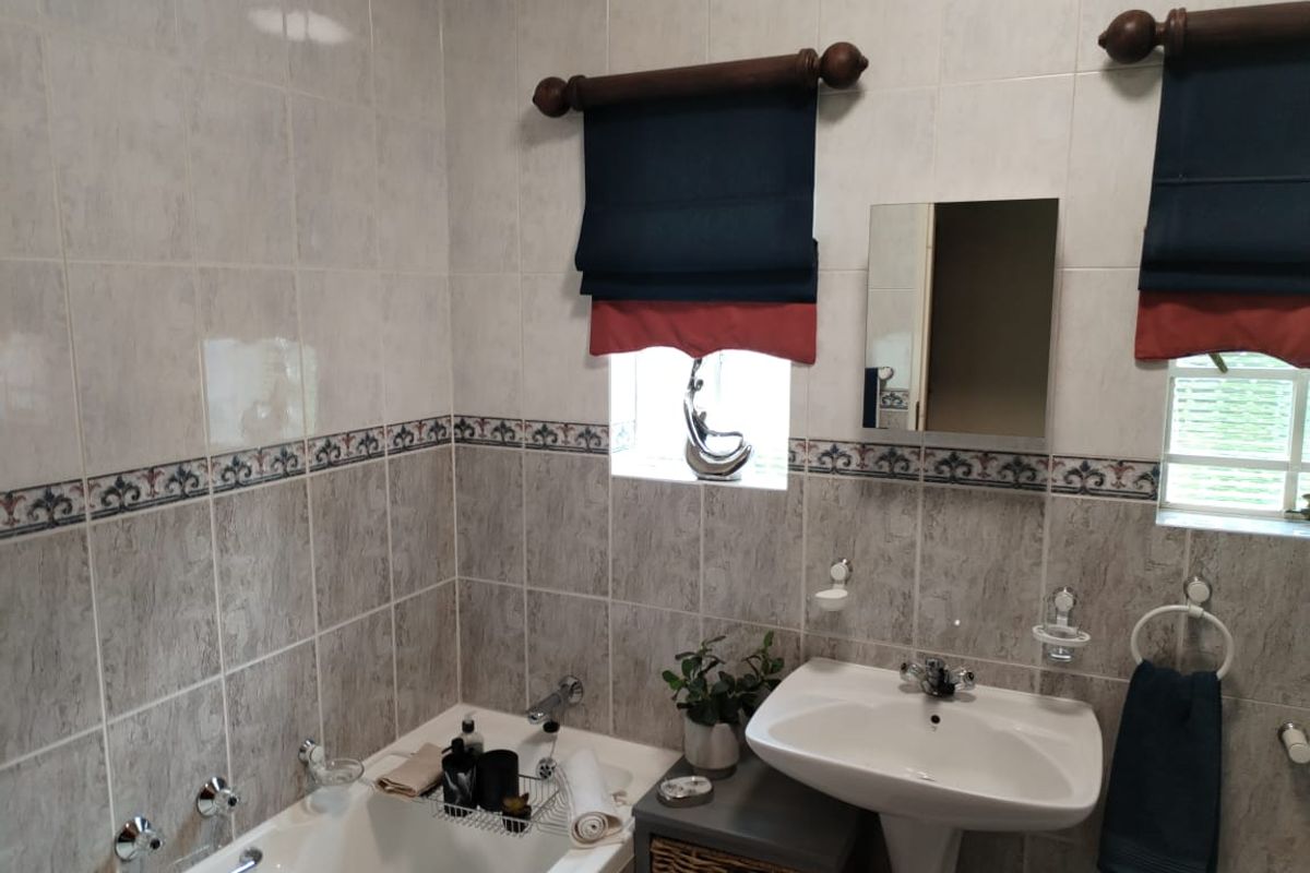 A functional bathroom featuring a built-in bathtub, pedestal sink, and tiled walls with decorative border accents.