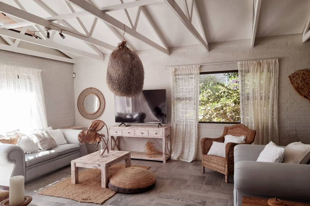 Spacious living room featuring exposed white timber roof trusses, tiled flooring, and large windows allowing for ample natural light.