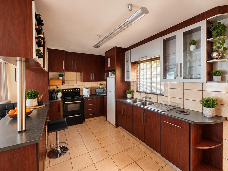 A functional kitchen featuring dark wood cabinetry, tiled backsplash, double basin sink, and integrated storage solutions with a breakfast bar area.