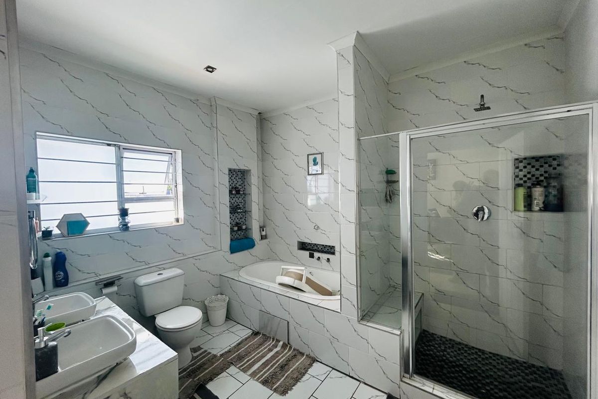 Modern bathroom featuring a glass-enclosed shower, built-in bathtub, dual vanity sinks, and marble-effect wall tiling.