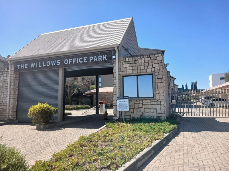 The main entrance to The Willows Office Park, featuring a secure gated access point, stone-clad guard house, and paved driveway.