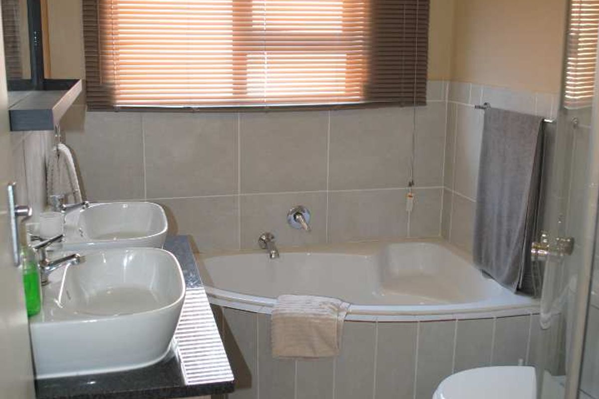 A functional bathroom featuring a corner bathtub, dual vessel sinks on a vanity, and a separate shower enclosure with neutral tiling.