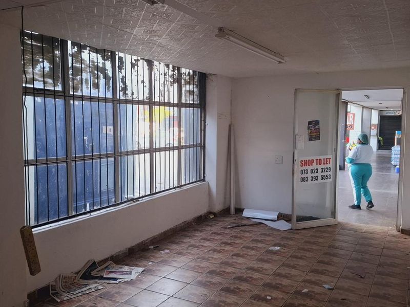 Vacant commercial retail space featuring tiled flooring, security bars on windows, and fluorescent lighting, currently requiring maintenance and refurbishment.