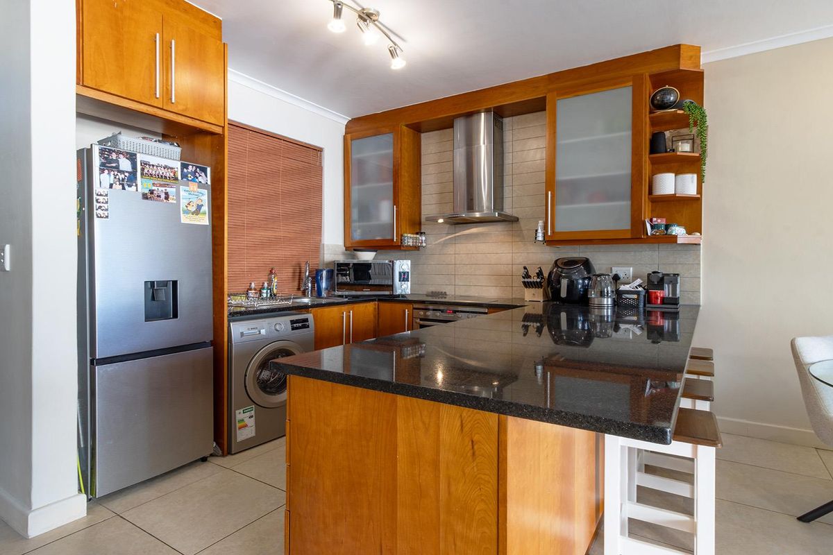 A functional kitchen featuring wooden cabinetry, granite countertops, a stainless steel extractor fan, and a tiled backsplash with integrated laundry and appliance space.