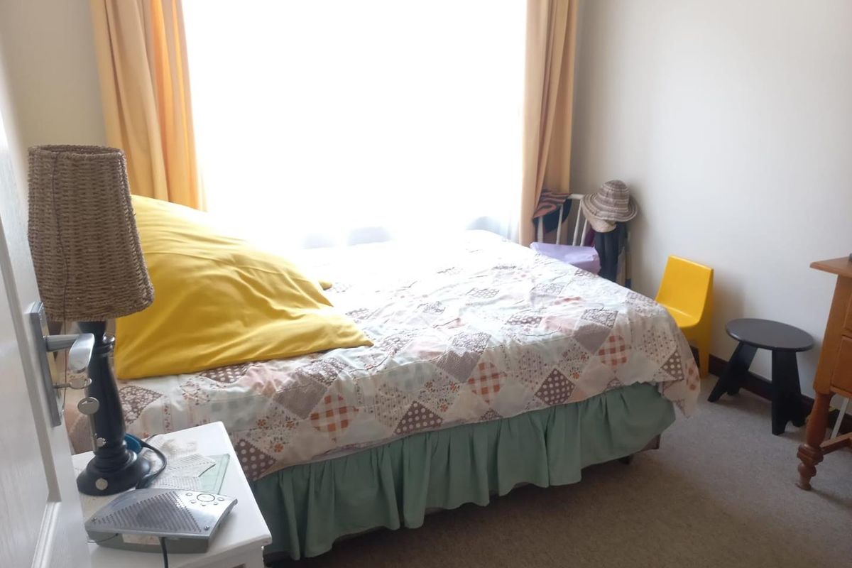 A bedroom featuring neutral walls, carpeted flooring, and a large window allowing for natural light.