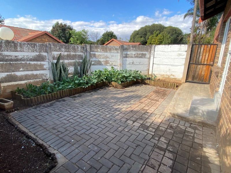 A private rear courtyard featuring paved flooring, raised garden beds, and a secure boundary wall with a timber access gate.