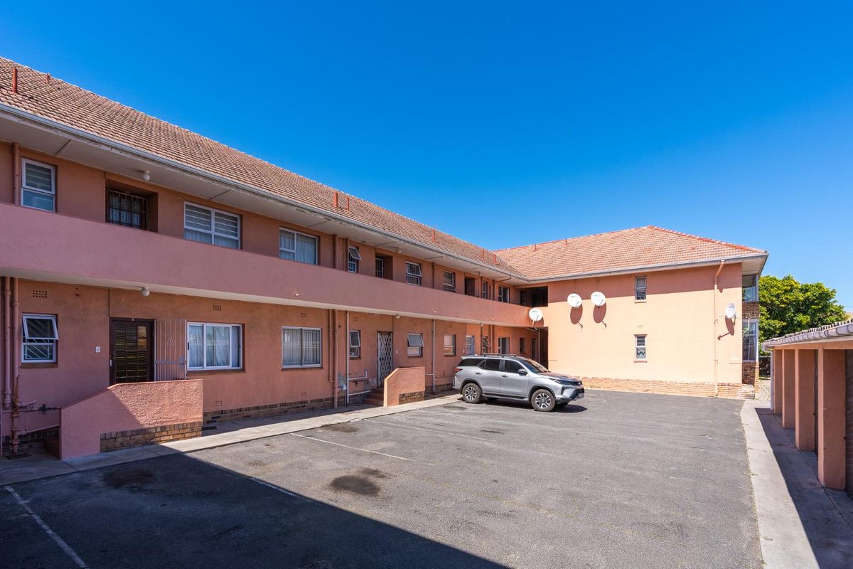 Exterior view of the apartment complex featuring a paved parking area, covered walkways, and traditional tiled roofing.
