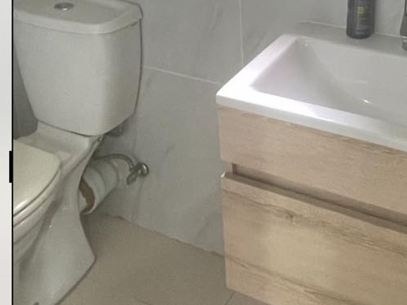 A modern bathroom featuring a wall-mounted vanity with a ceramic basin and a standard toilet, finished with neutral wall and floor tiles.