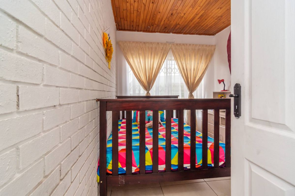 A bedroom featuring a white painted brick wall, tiled flooring, and a timber-clad ceiling.