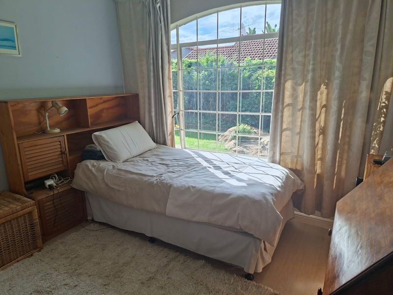 A cozy bedroom featuring a large arched window that provides ample natural light and a view of the garden.