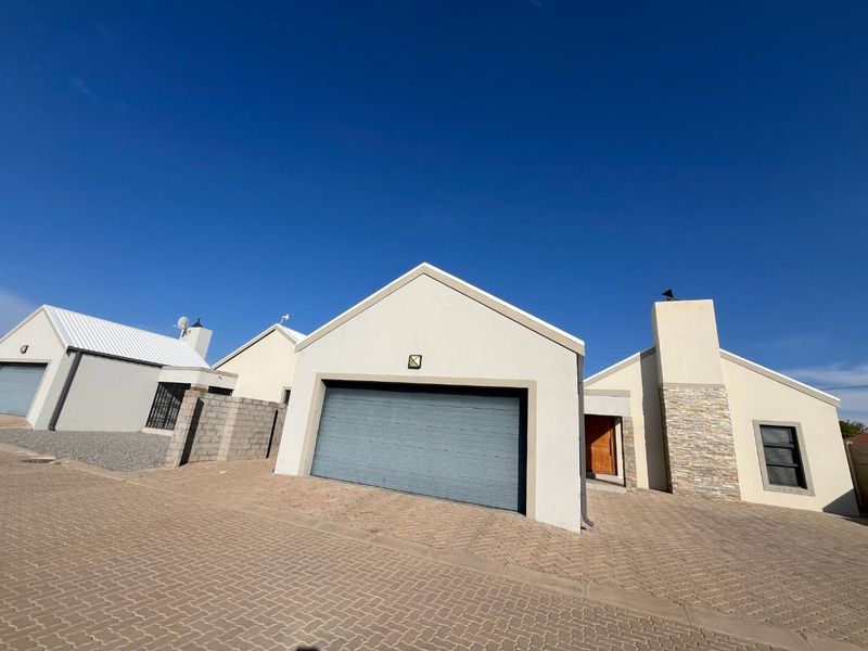 Front exterior view of a residential property featuring a paved driveway, a modern sectional garage door, and decorative stone cladding on the chimney.