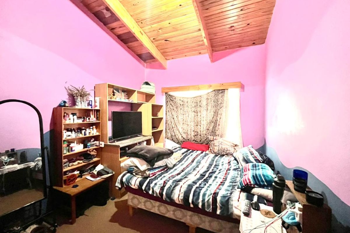 A bedroom featuring a vaulted timber-paneled ceiling and pink painted walls, providing a functional sleeping space with potential for cosmetic updates.