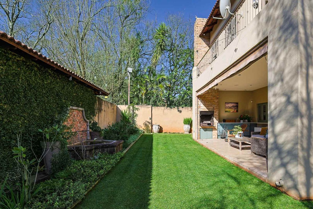 A well-maintained rear garden featuring a manicured lawn, a stone water feature, and a covered patio area with a built-in braai.
