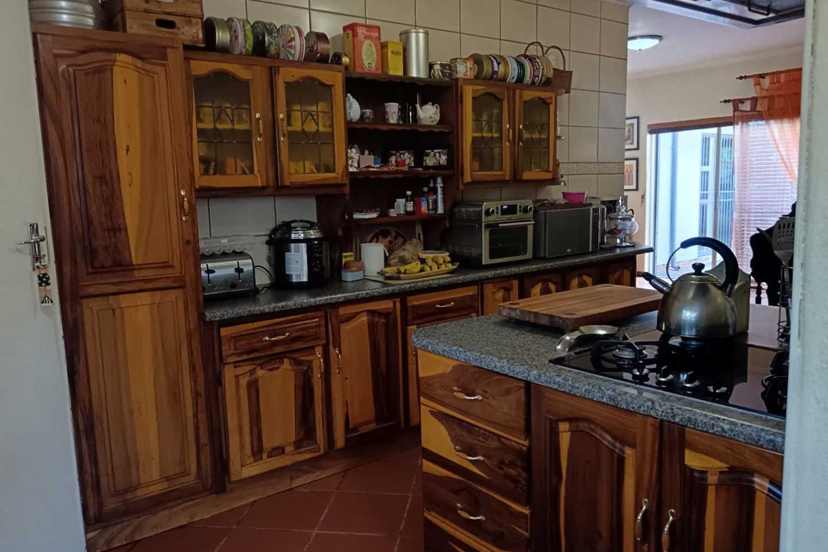 A functional kitchen featuring solid wood cabinetry, granite-look countertops, a built-in gas hob, and tiled flooring, offering a traditional aesthetic.