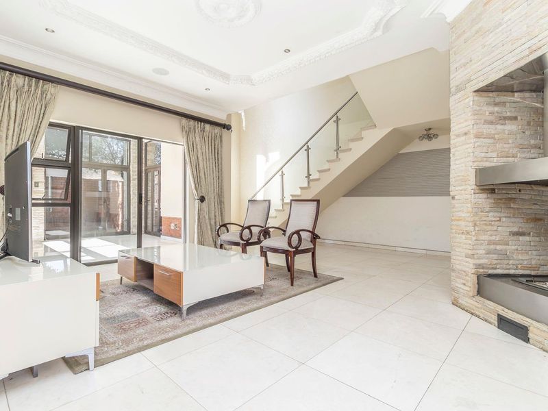 Spacious living room featuring a prominent stone-clad fireplace, tiled flooring, decorative ceiling details, and a modern staircase with a glass balustrade.