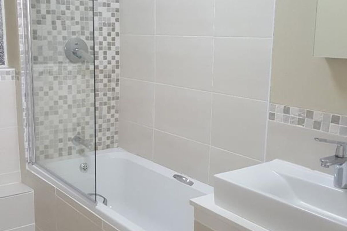 A clean, modern bathroom featuring a bathtub with a glass shower screen, mosaic tile accents, and a sleek vanity basin.