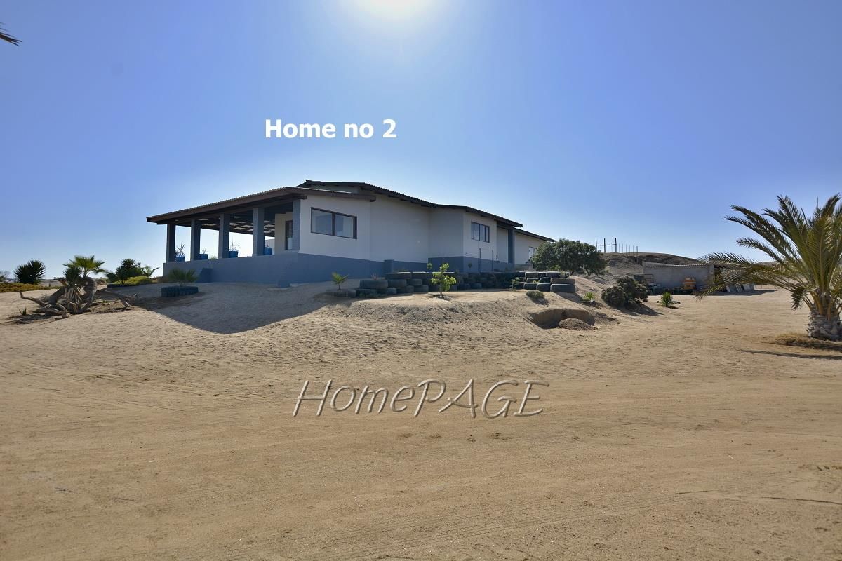 Exterior view of a detached dwelling on a small holding, featuring a covered patio area and expansive sandy grounds.