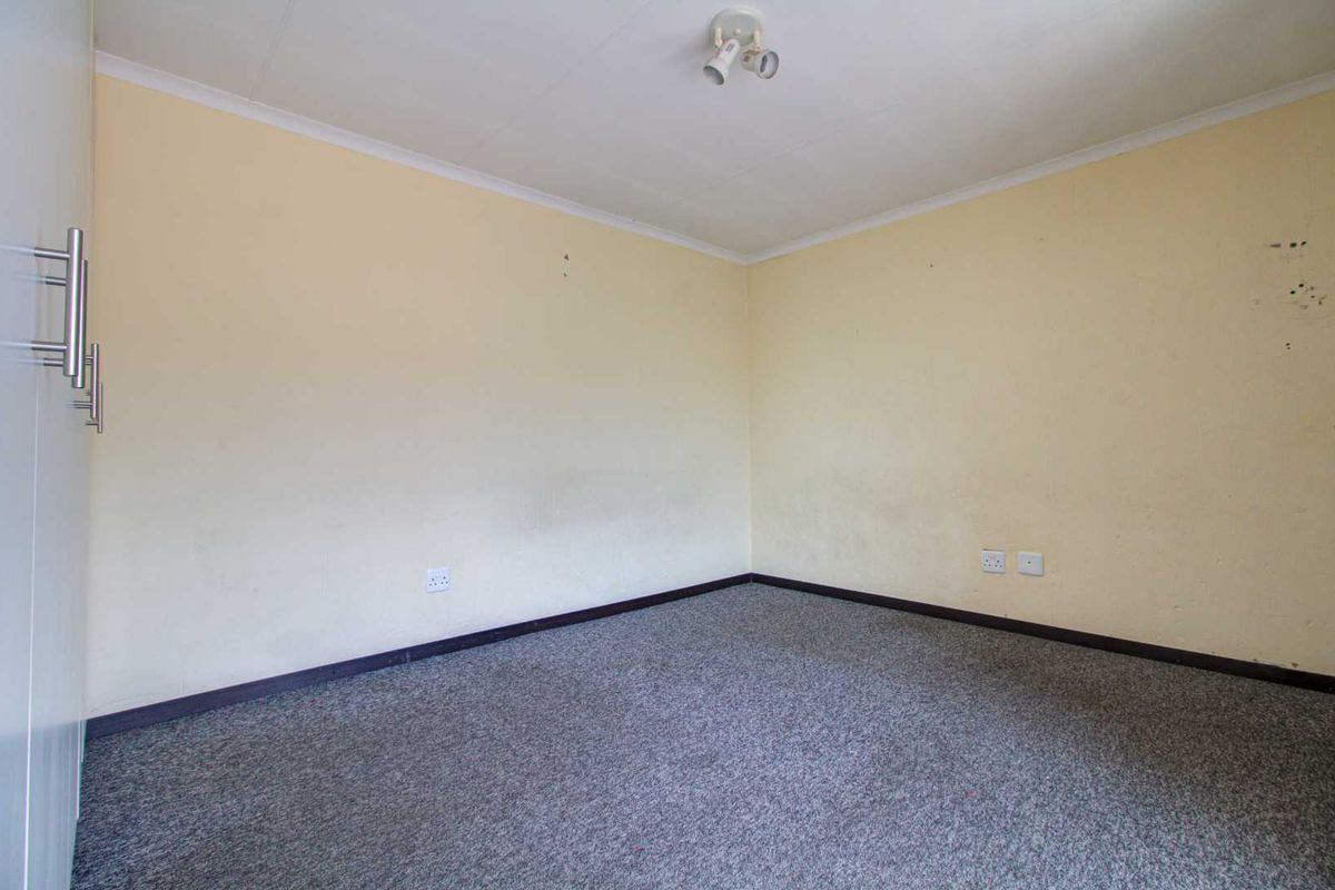 An empty bedroom featuring neutral wall paint, grey carpeting, and built-in cupboard storage.
