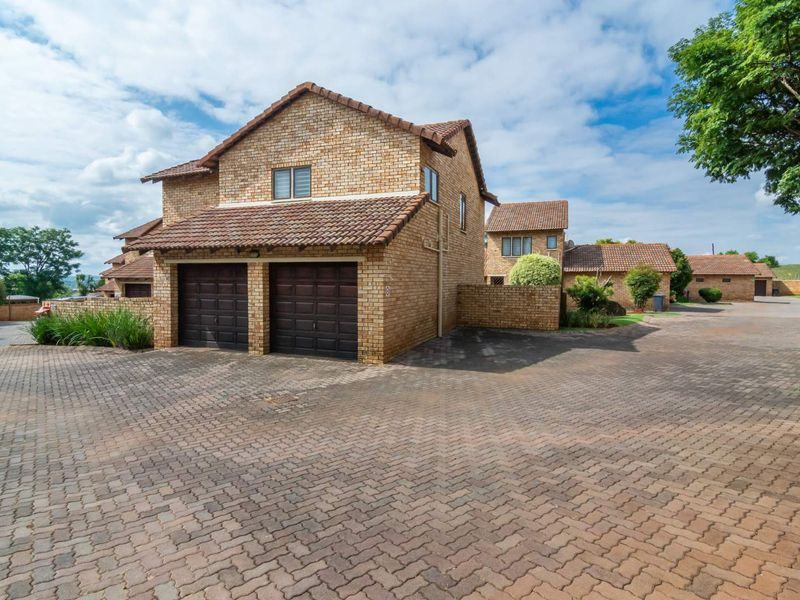 Exterior view of a facebrick townhouse featuring a double garage and extensive paved driveway within a residential complex.