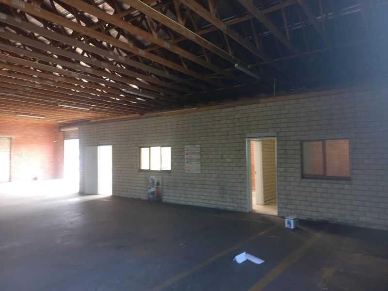 Spacious industrial utility area featuring exposed timber roof trusses, concrete flooring, and cinder block walls with multiple internal access points.