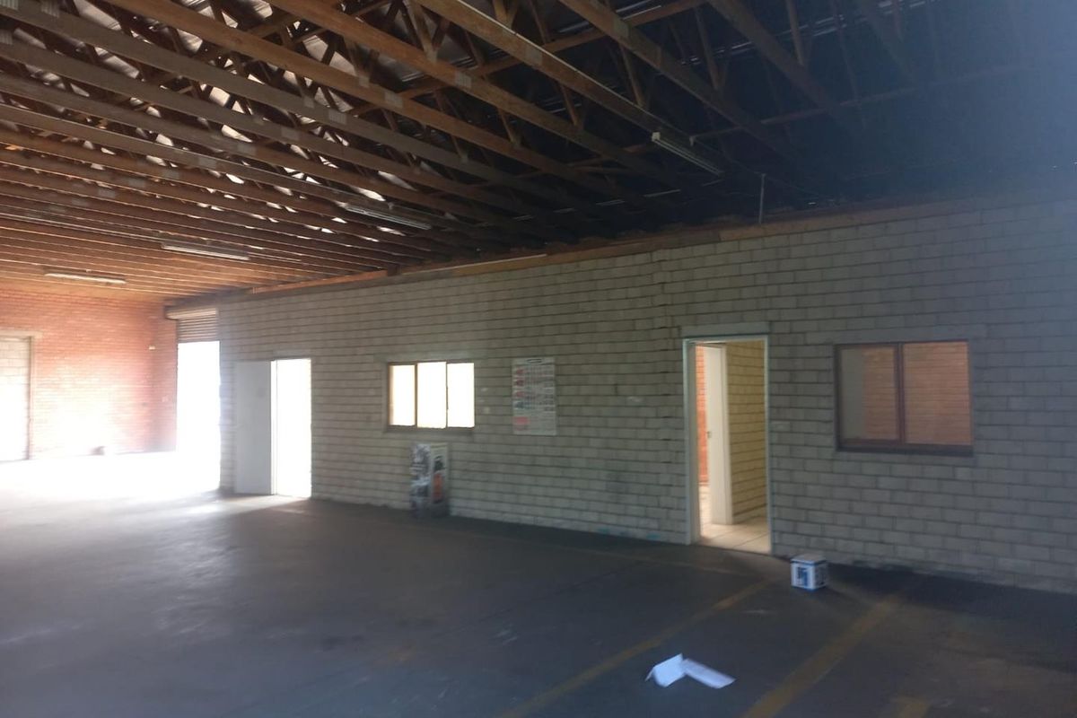 Spacious industrial utility area featuring exposed timber roof trusses, concrete flooring, and cinder block walls with multiple internal access points.